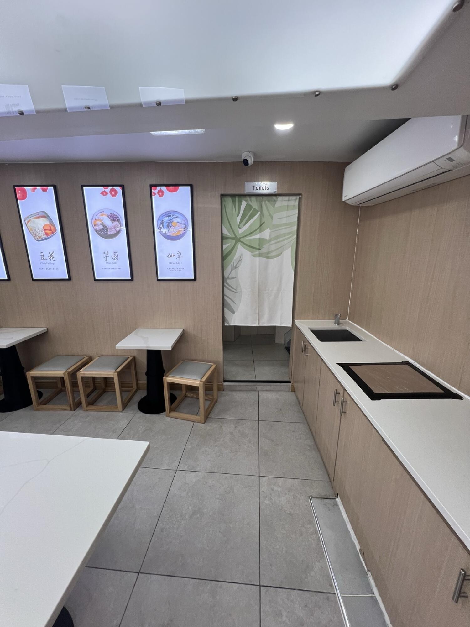 Tables and stools along left. Toilet doorway in centre. Counter with sink along right.