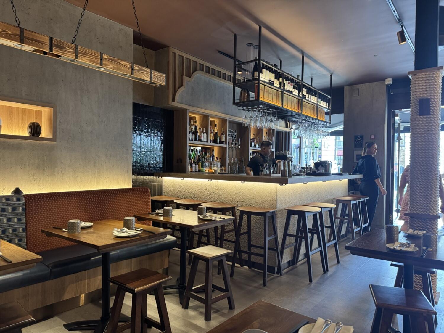 Half booth along left wall. Bar counter and stools in centre. Tables and chairs on right.