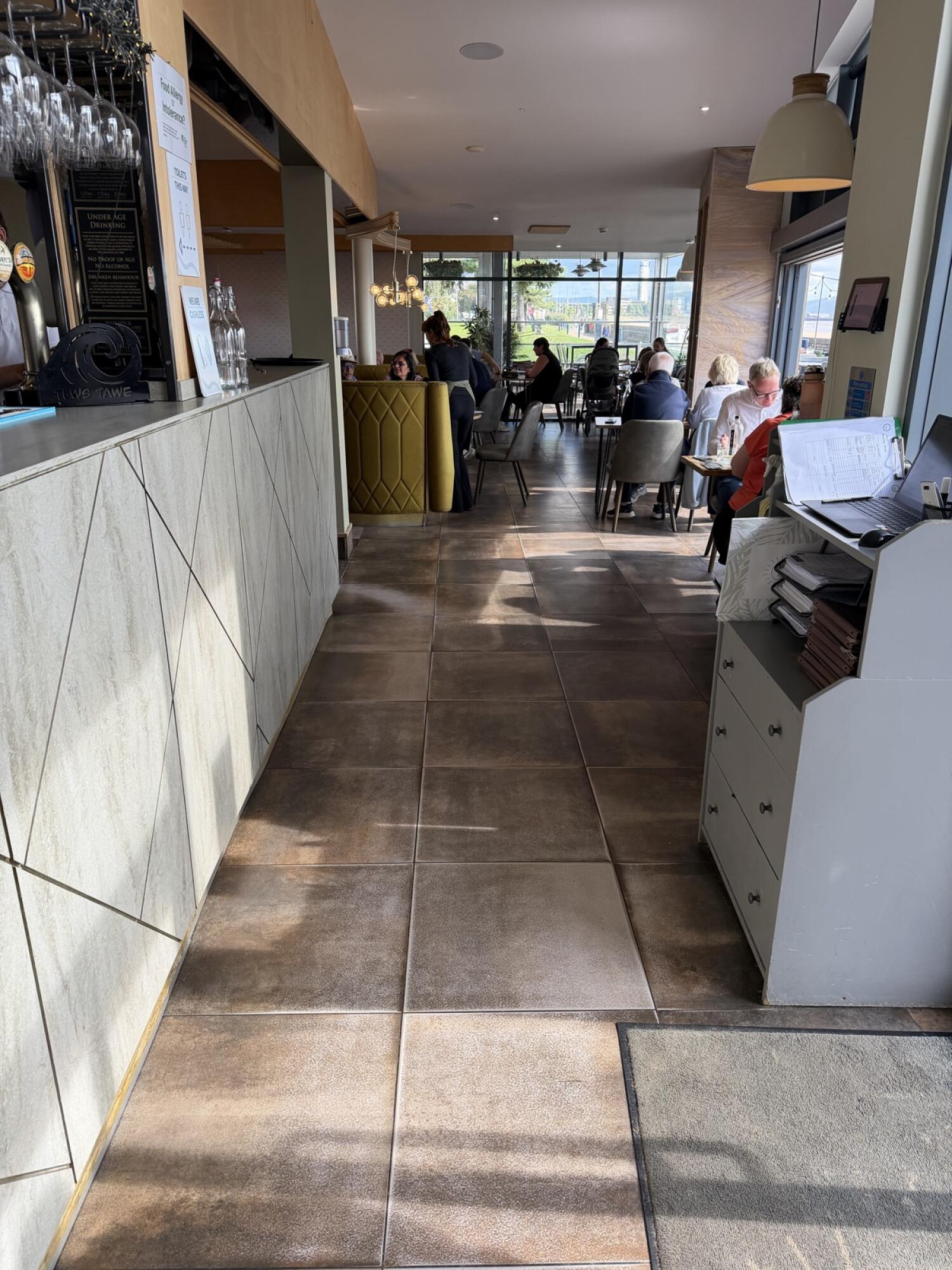 Bar counter along left. Tiled path through centre. Tables and chairs along right.