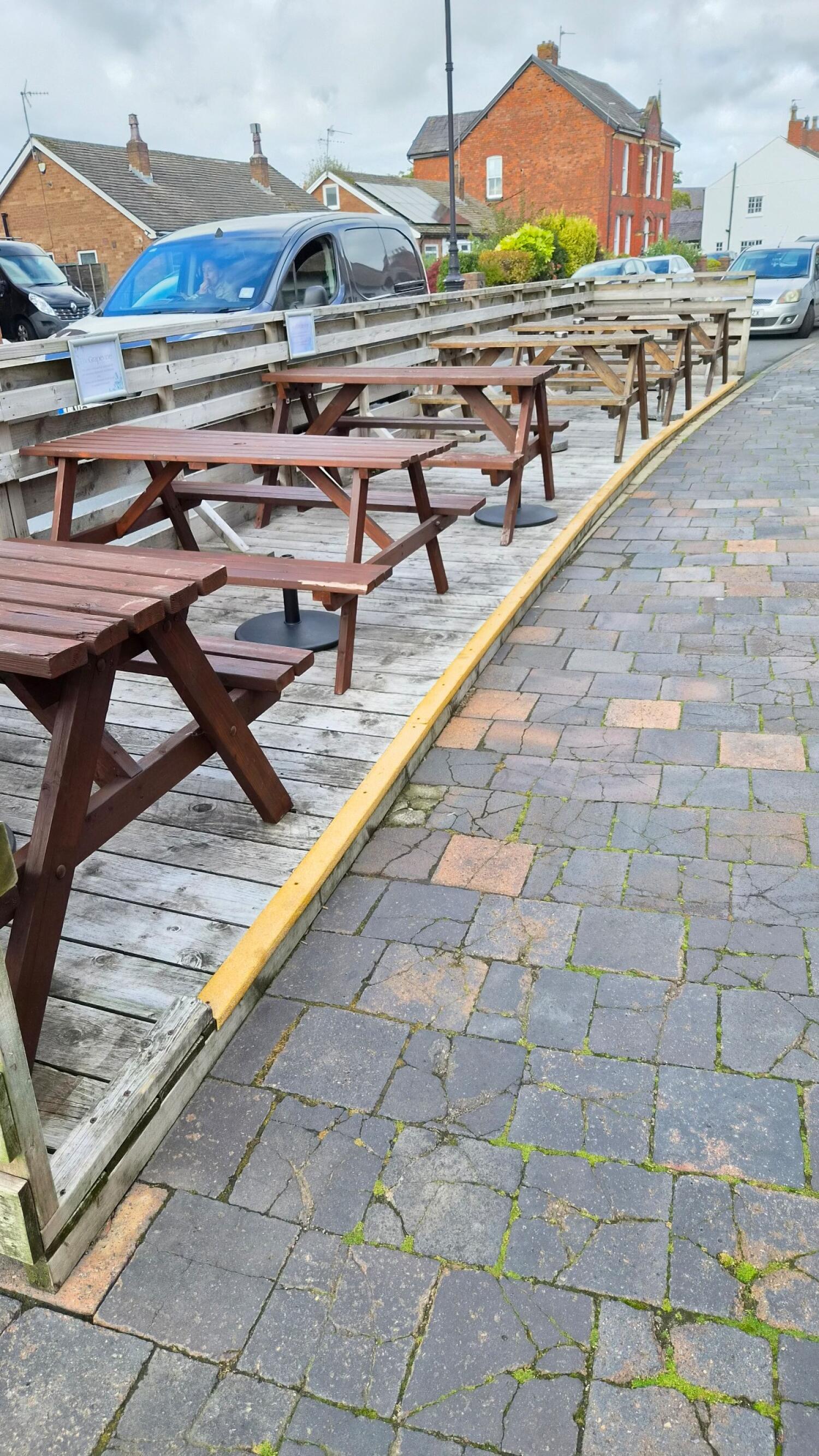 Picnic tables on wooden decking left. Raised edge beside paved path right.