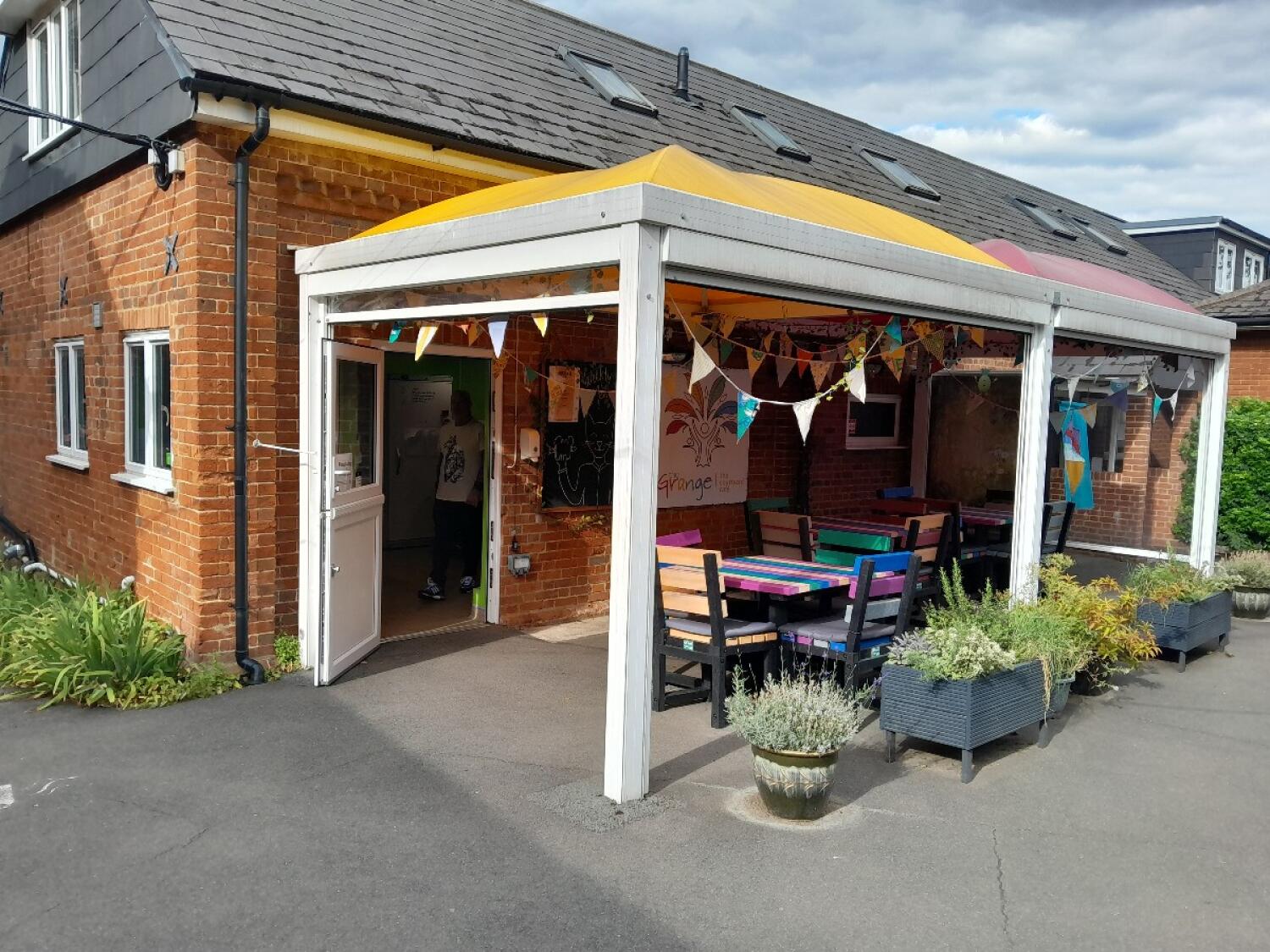 Entrance door on left. Covered tables and chairs centre. Planters along right.