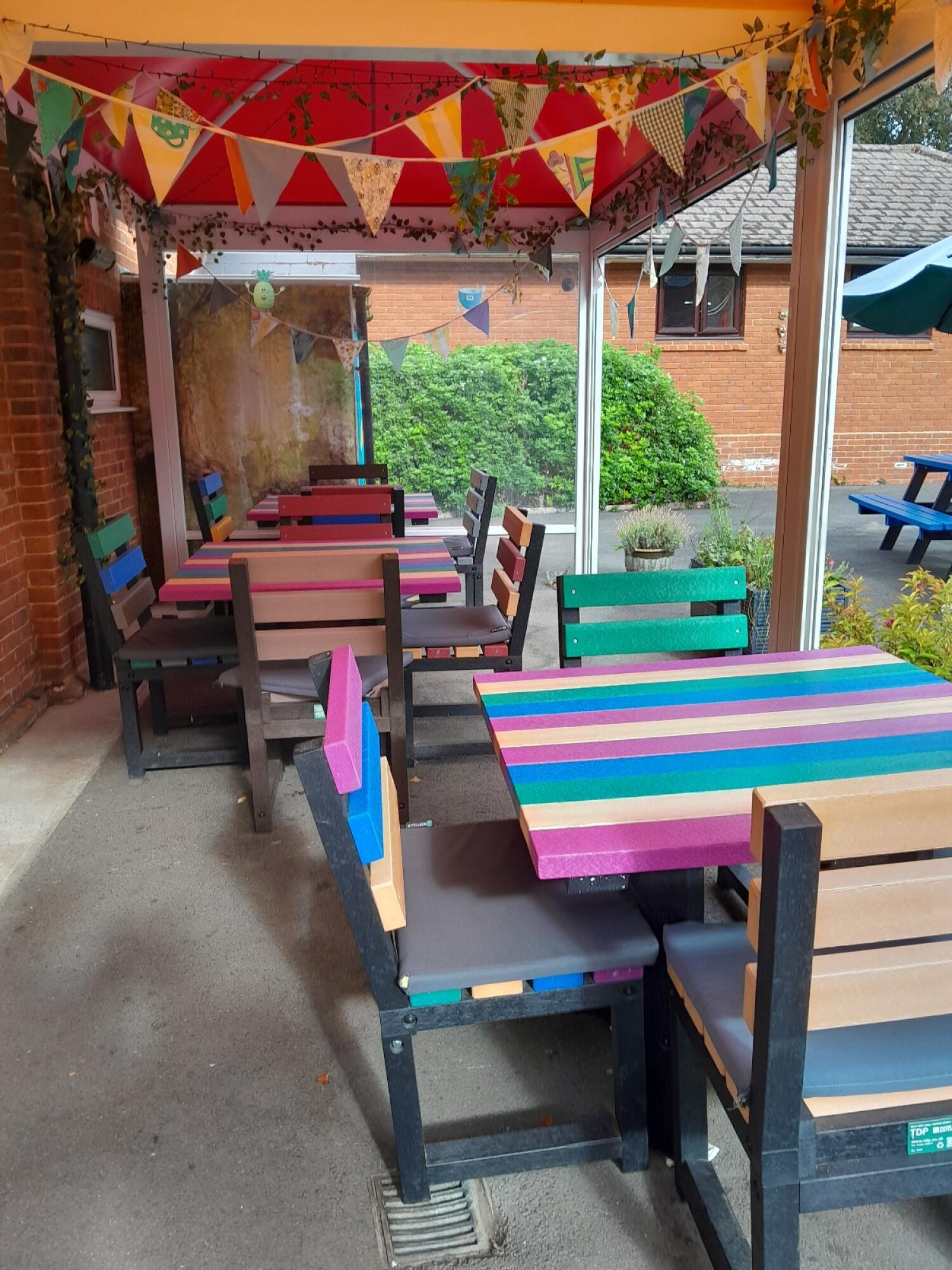 Benches and tables along left. Drain in centre walkway. More benches and tables right.