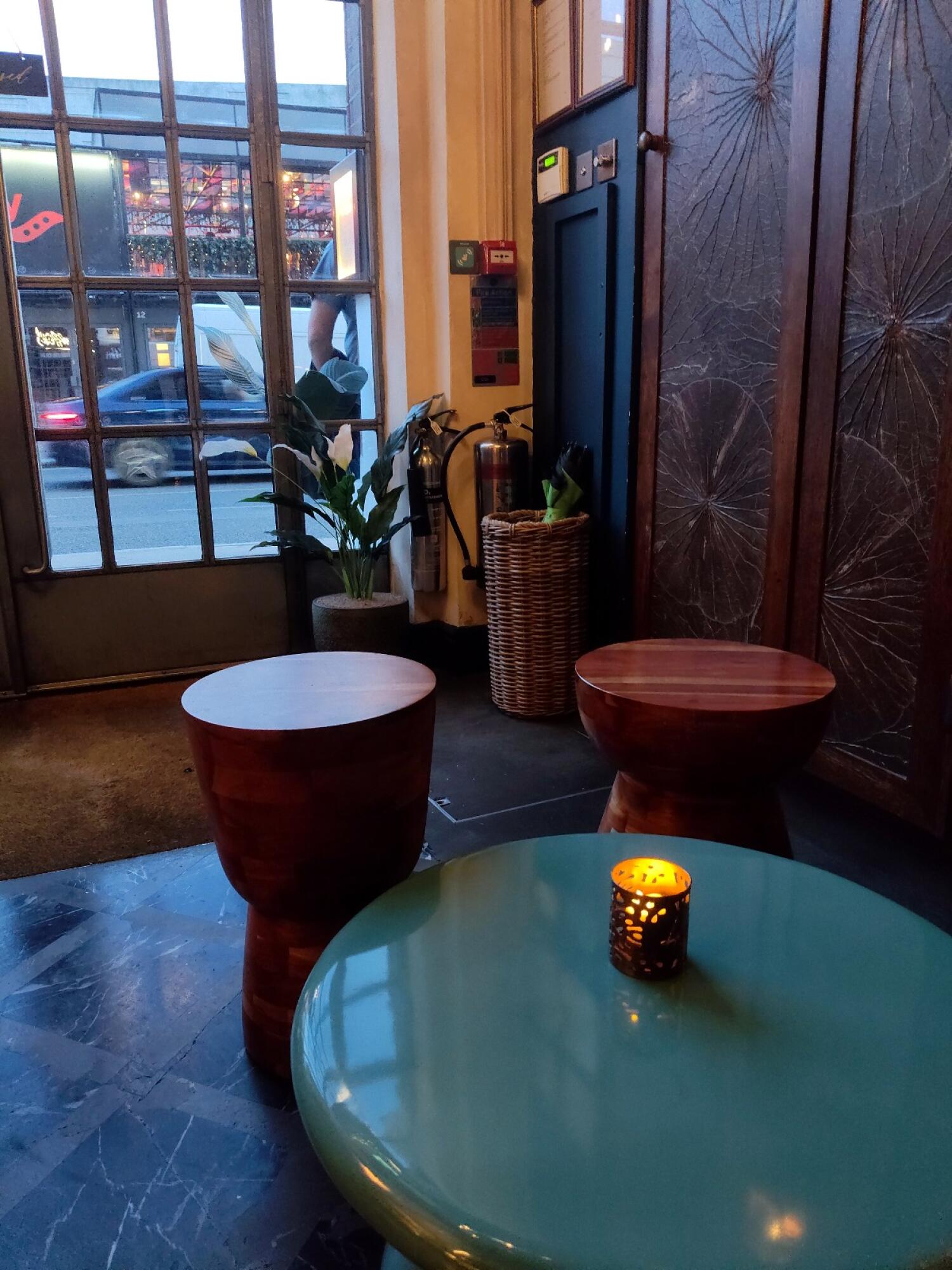 Glass entrance on left. Tables and stools in centre. Table and stool on right.