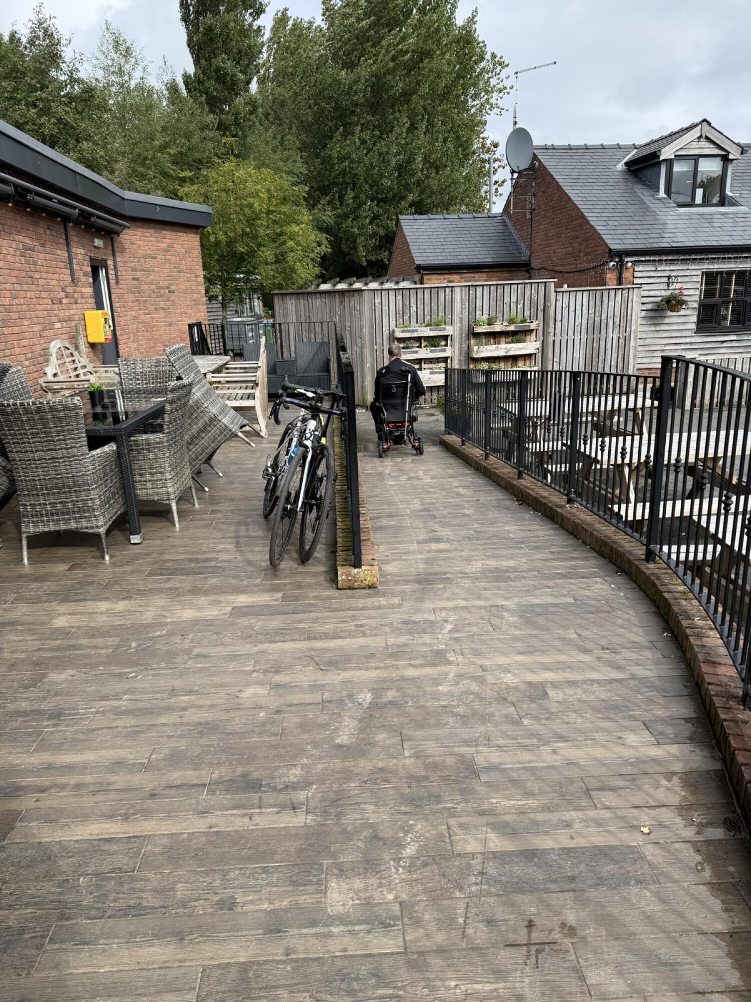 Tables and chairs along left. Bicycle beside sloped centre path. Railings along right.