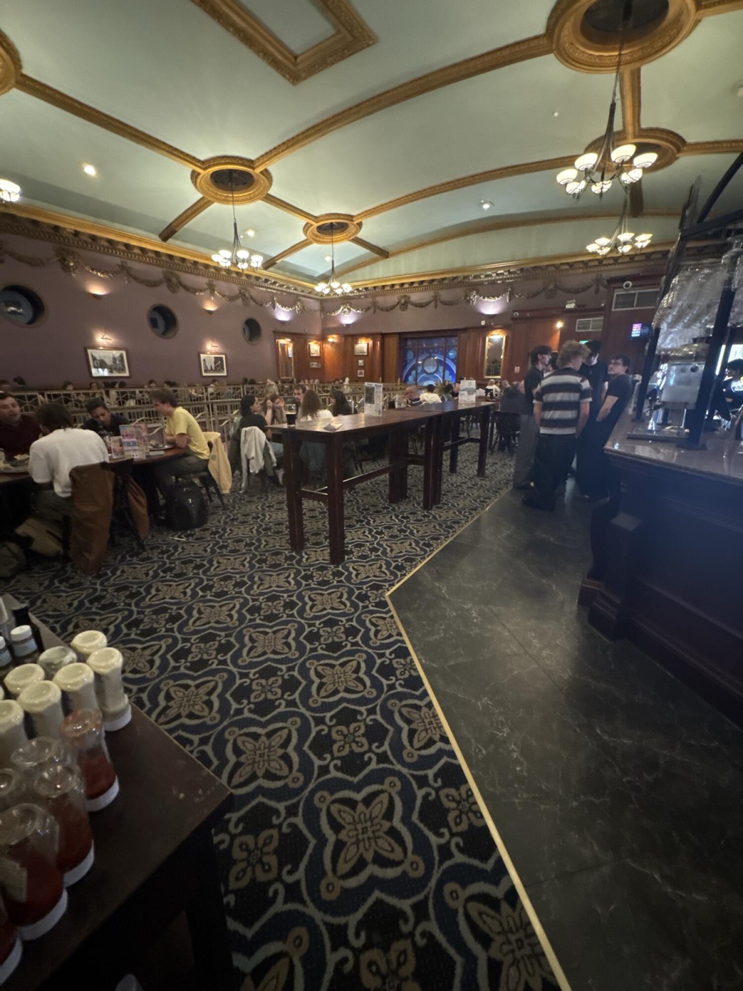 Tables and chairs along left. High tables in centre. Bar counter and tiled walkway right.