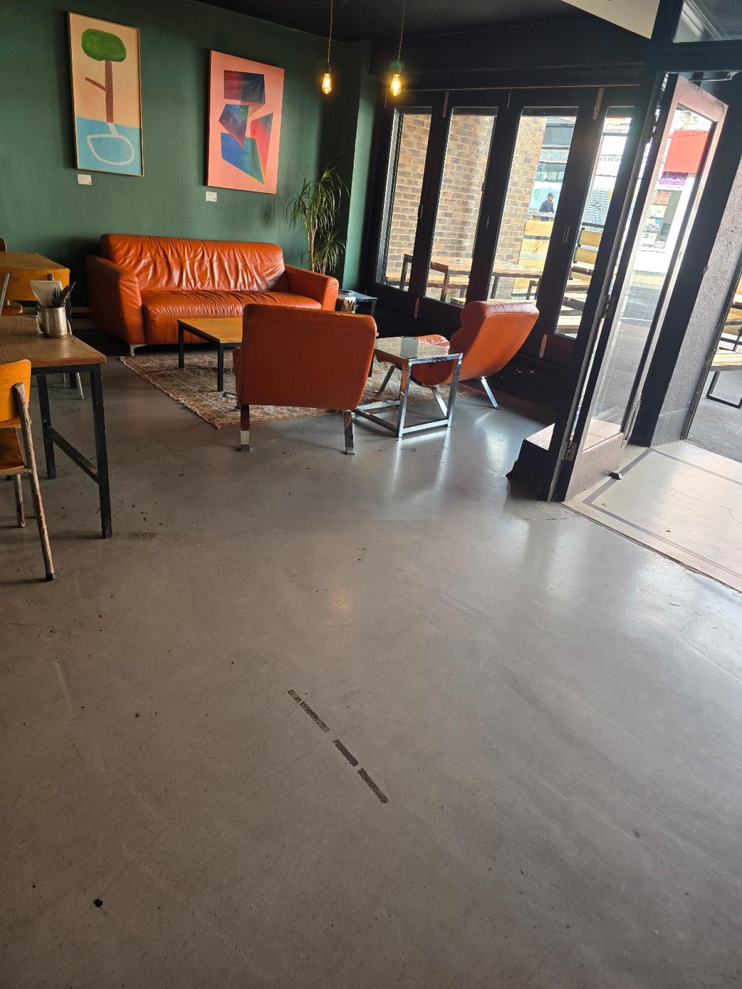 Tables and chairs along left. Sofa seating in centre. Entrance doors along right.