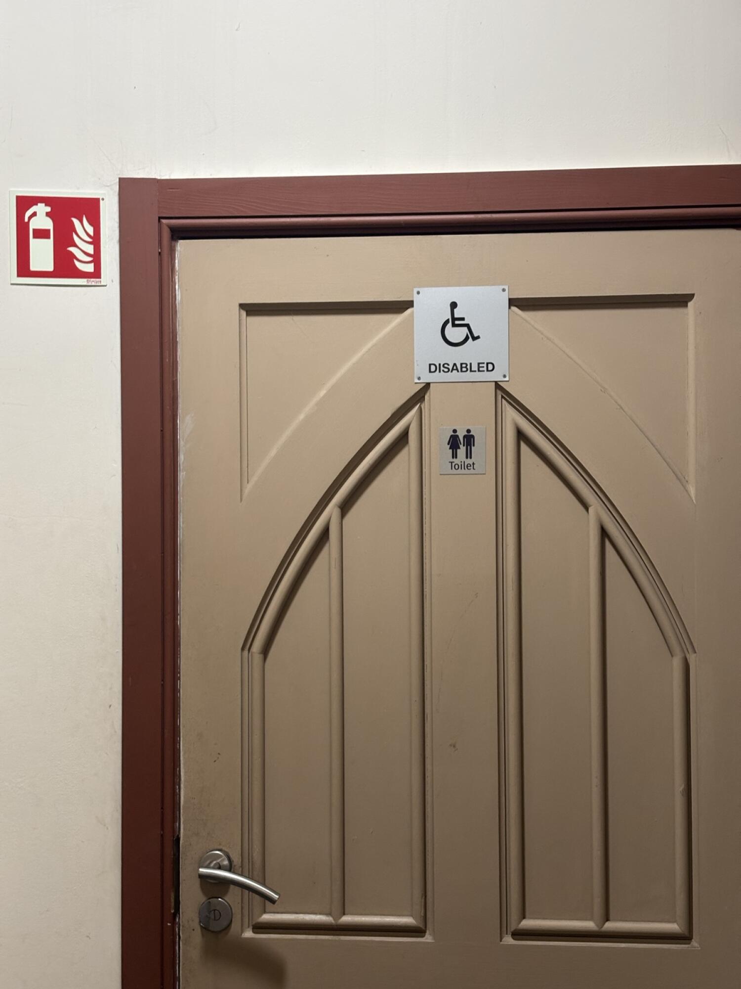 Beige wooden toilet door. Use handle to open.