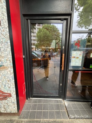 Glass door with black frames. Push from right handle to open. A slope up to door.