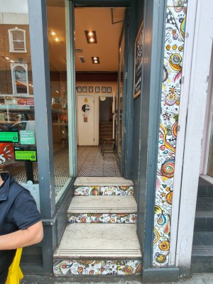Facing entrance. Three steps up to access the door. Grey framed door. Push handle on left to open.
