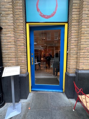 Glass door with blue and yellow frame. Push golden handle on left to open.