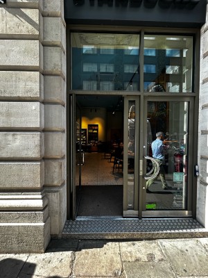 Two glass doors with black frames ahead. Door on left opens with curved silver handle on right. Push to open.