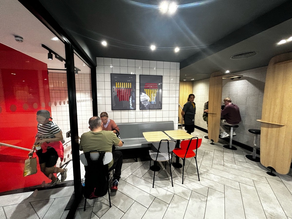 From door, facing left. Glass wall on left. Half booth ahead with chairs. Path on right leading to more seating.
