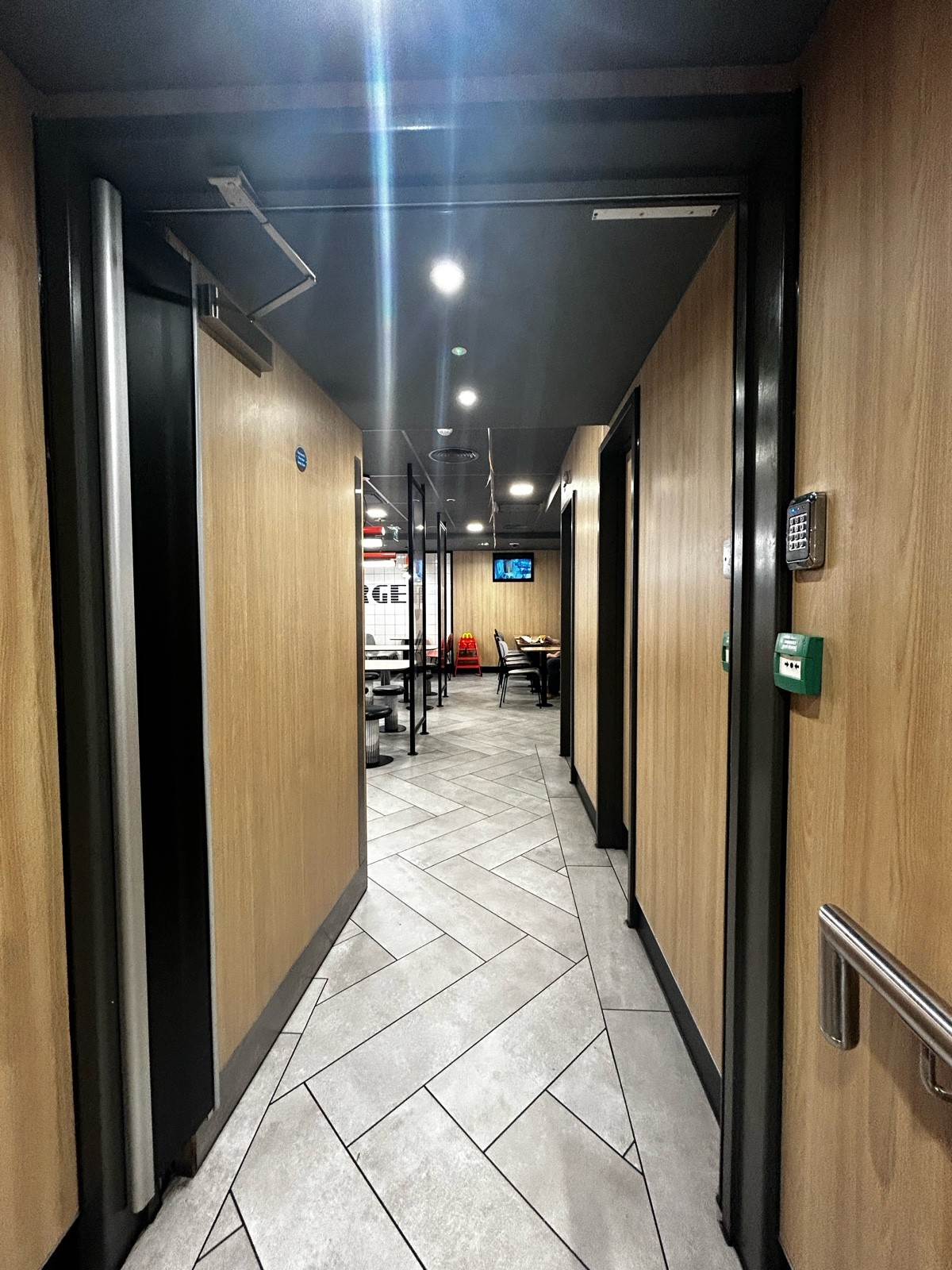 From end of steps, facing straight. Wooden preceding door ahead. Silver pad on mid right. Push to open