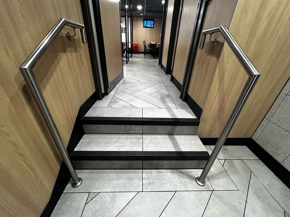 From path, facing straight. Two steps ahead leading to more seating area and preceding wooden door. Handrails on both sides