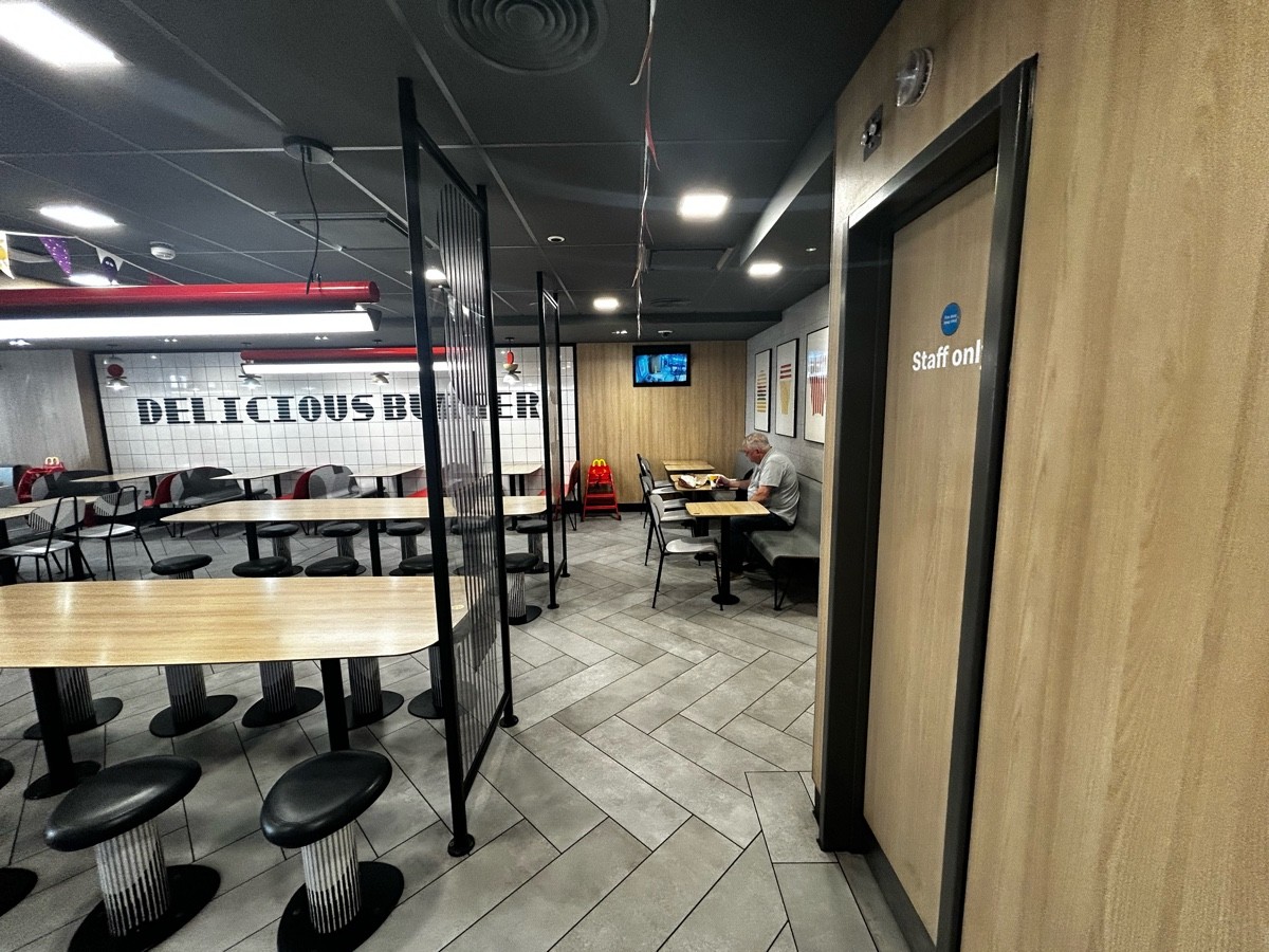From preceding door, facing straight. Stools and long tables with glass panels on their right on left. Path ahead leading to half booths on right.