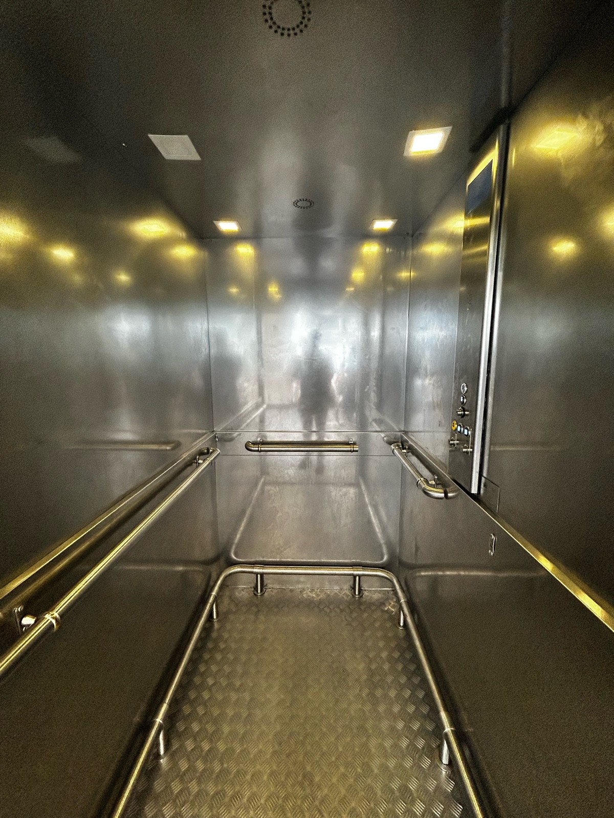 From door of lift, facing straight. Handrails on left, ahead and right of inside of lift.