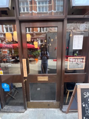 Single glass door with brown frame. Push from left of door to open.
