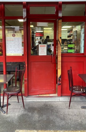 Red door with glass panel ahead. Push door to open via red handle on right. Outdoors seating on both sides of door.