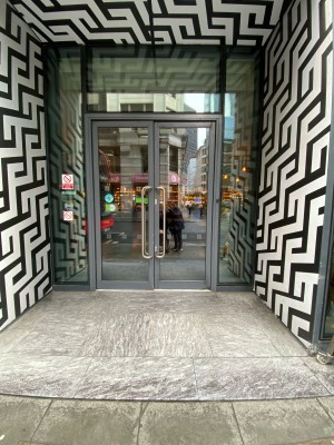 Glass doors with grey frame ahead. Pull from metal handles in centre to open.