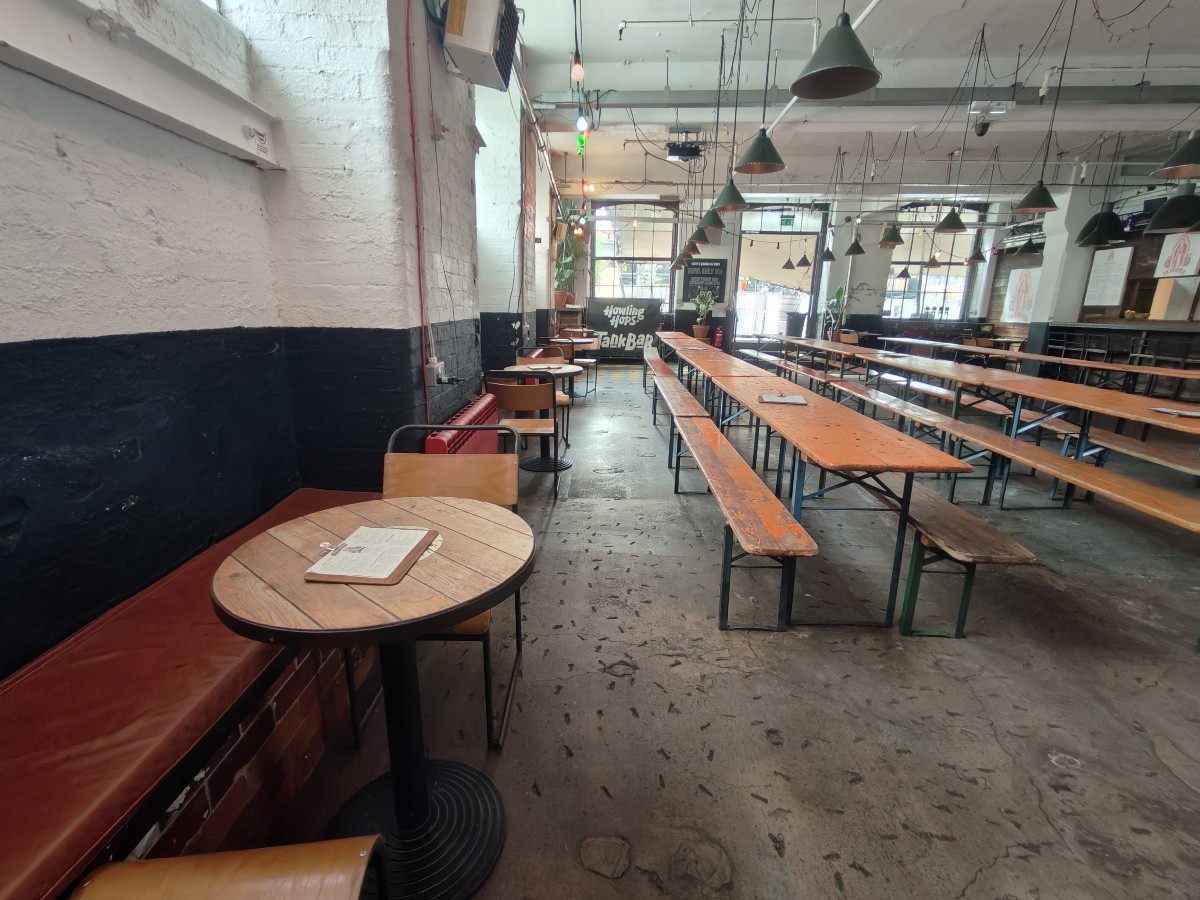 From end of bar facing right. Half booth on left. Tables and chairs behind along left wall. Rows of tables and benches on right.