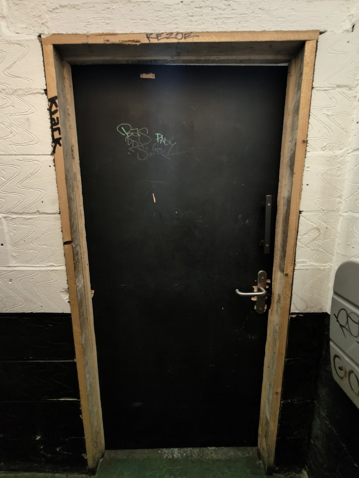 Back of door. Push silver handle on right to open.