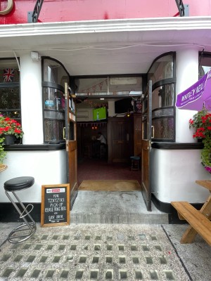 Facing entrance. Path ahead. Outdoor seating either side. One step at end of path. Wood-panelled glass doors ahead. Pull handles at centre to open.