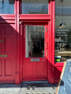 Single red wooden door with large glass panel and gold metal vertical handle on right. Push to open.