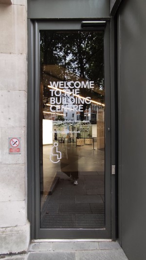 From sidewalk facing venue. Glass door with black frames ahead. Press button on right to open door.