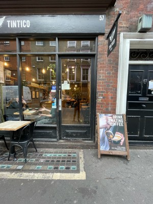 Black wood-framed glass door ahead. One step before door. A-board on right.