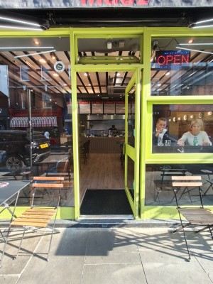 Facing green framed single glass door. Push green metal leaf on left to open.
