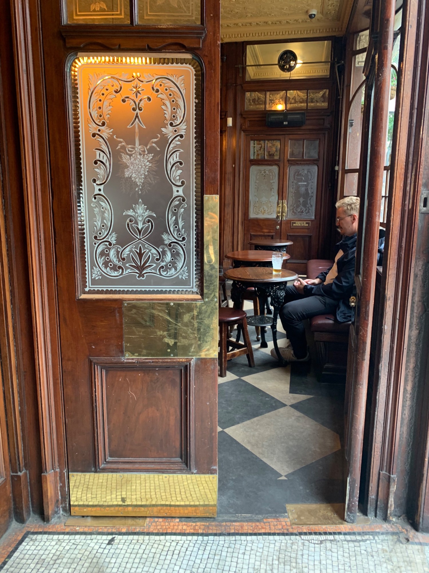 From left foyer, looking right. Doorway to main area ahead. Double brown wooden doors with glass panels. Push from center to open.