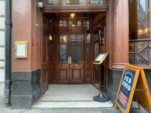 From street, facing entrance. Path center to main entrance ahead. Slide wooden folding doors from right to left. Two signs along right of path.
