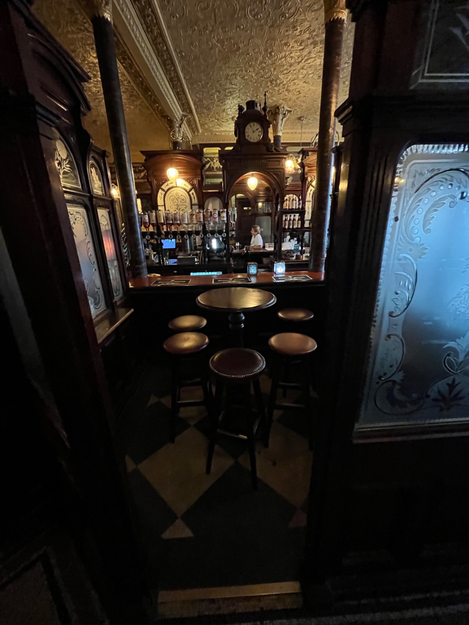 From further along path facing right. Open archway ahead. High table with stools through archway. Bar along back wall.