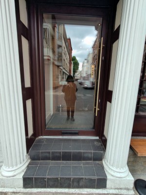 Facing black framed entrance door. Push golden metal grab rail on right to open.