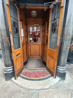 Facing wooden framed entrance door. Pull golden metal handles in centre to open.