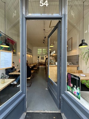 Glass door with grey doorframe. Push gold pad on left to open.