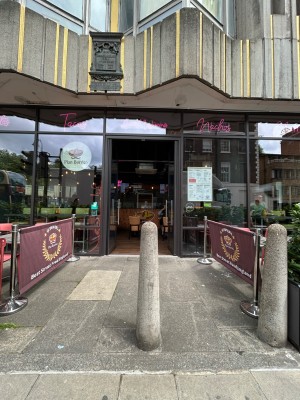 From street, facing venue. Path ahead leads to entrance on back wall, obstructed by bollard.