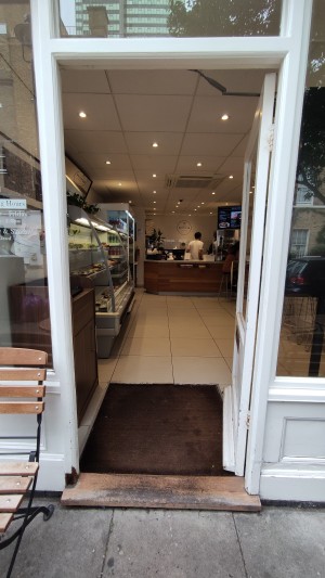 Glass door with white frames ahead. Push to left via vertical golden handle to open.