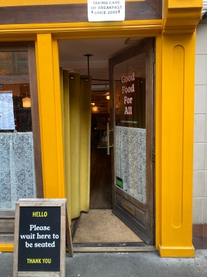 Facing single glass door with wooden frame. Push open via metal handle on left.