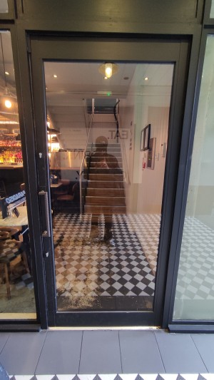 Glass door with black frames ahead. Push to left via vertical brass handle to open.