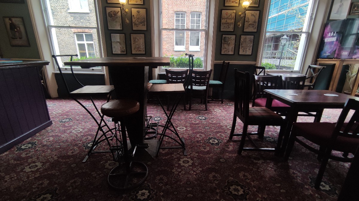 From top of staircase facing straight. Path ahead along left and right. Table with chairs at back right. High table with stools on left.