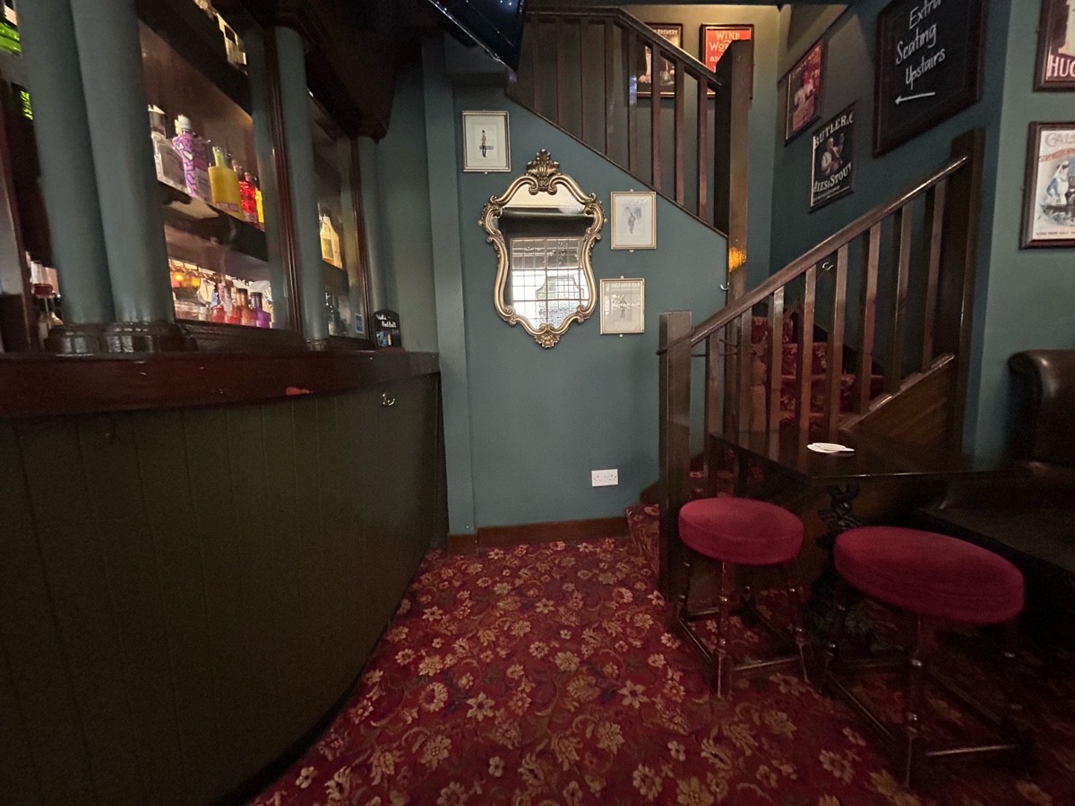 From end of bar facing left. Armchair, table and stools on right. Path middle to stairs back right.