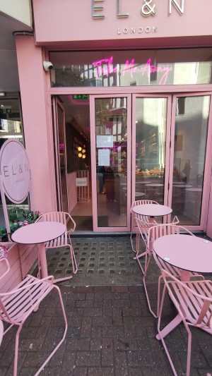 From pavement, facing straight. Path ahead to entrance. Outdoor tables and chairs on either side.