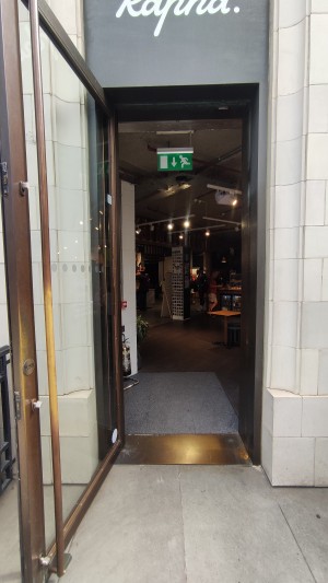 Glass door with bronze frames ahead. Pull via vertical bronze handle to right to open.