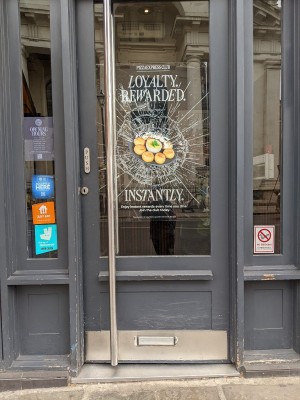 Glass door with grey frame and silver handle on left. Push to open.