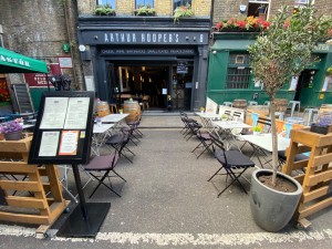 From street, facing venue. Menu stand on left. Plant on right. Path ahead in front.