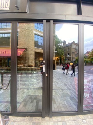 Glass double door, with black doorframe. Handles at centre. Push left door to open.