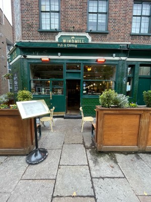 Path to main door ahead. Wooden planters on left and right. Menu stand on left.