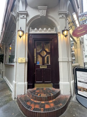 Facing wooden door with glass panels. Pull brass handles on left to open. Two steps up ahead of door.