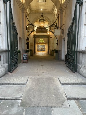 From street facing The Royal Exchange. Two steps up with ramp at centre. Dark green metal gates ahead of ramp.